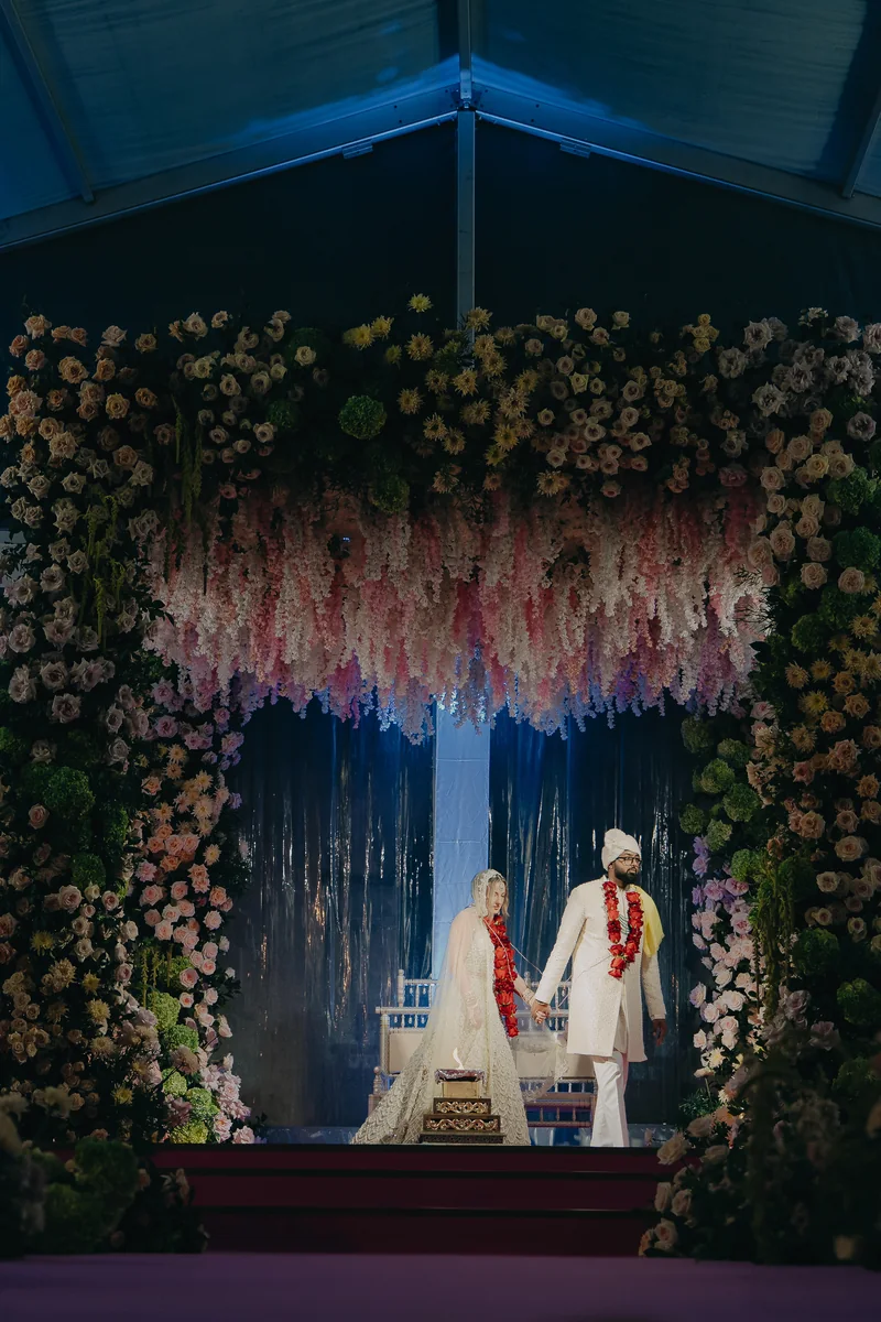 Megan and Karan standing beneath a floral wedding backdrop