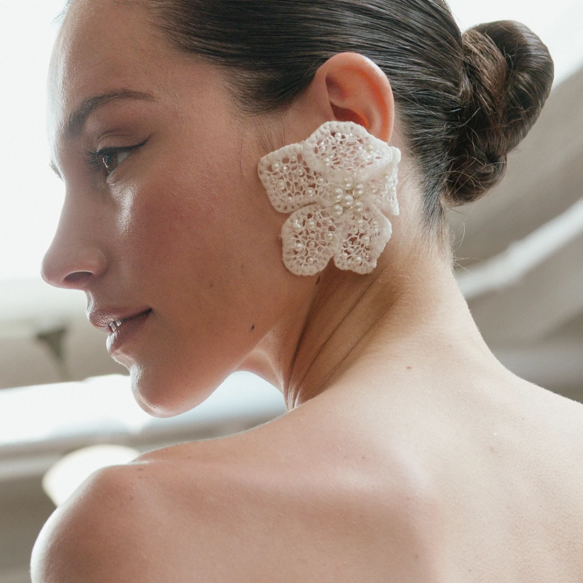 A tight side-profile view of the lace-and-pearl floral earring